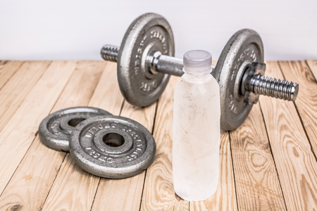 Dumbbells , weight plates and bottle of water on wooden background for bodybuilder. Concept for sport player or workout. gym of accessories for fitnessの写真素材