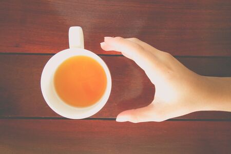 Hand with cup of tea on wood table,top viewの写真素材