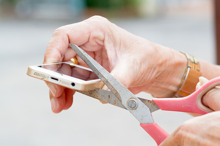 The old man's hand holding scissors and cut mobile phone.の写真素材