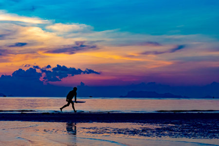 Silhouette of man with surfboard on the beach with twilight sky backgroundの写真素材