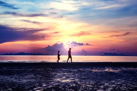 Silhouette of man with surfboard on the beach with twilight sky backgroundの写真素材