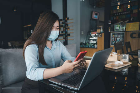 Asian woman wearing a mask uses a smartphone in a coffee shop.の写真素材