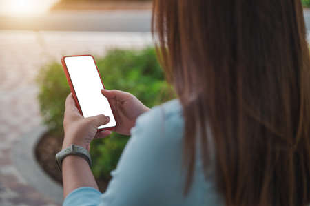 woman using a smartphone in a park, a blank smartphone screen, perspective taken from behind a person.の写真素材