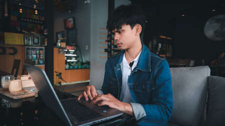 Man asian office worker of Thai descent is typing and working with notebooks in a coffee shop during the day.の写真素材