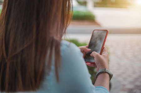 woman using a smartphone in a park, a blank smartphone screen, perspective taken from behind a person.の写真素材