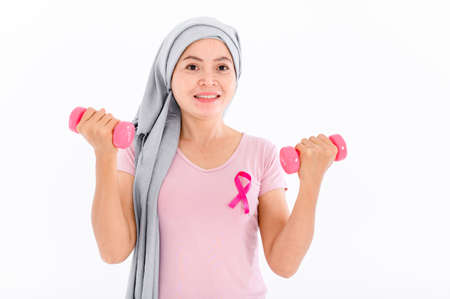 Asian women muslim religious women in hijab attach a pink ribbon to their tops. Doing exercise by lifting pink dumbbells.  breast cancer concept, cancer prevention concept. Acne and dark spots.の写真素材