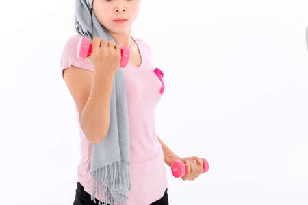 Asian women muslim religious women in hijab attach a pink ribbon to their tops. Doing exercise by lifting pink dumbbells.  breast cancer concept, cancer prevention concept. Acne and dark spots.の写真素材