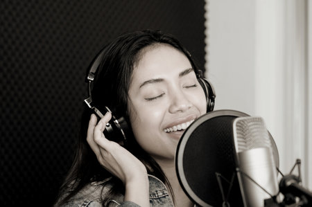 Asian female singer singing in a recording studio. Female singer singing and playing guitar.の写真素材