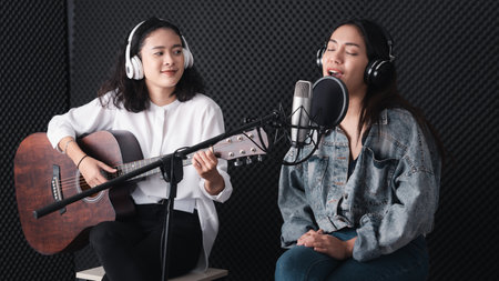 Asian female singer with a passion for music and microphone. While playing her guitar in a professional studio. Music concept, sound recording concept.の写真素材