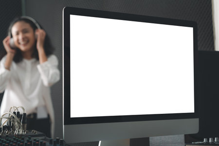 An empty computer screen in the recording room. Behind an Asian woman stood singing with passion and recording equipment.の写真素材