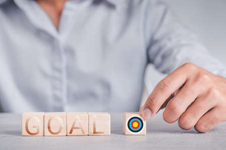 Businessmen wear a white shirt at their desks in the office. Use your hand to pick up a wooden cube inscribed with the word goal.の写真素材