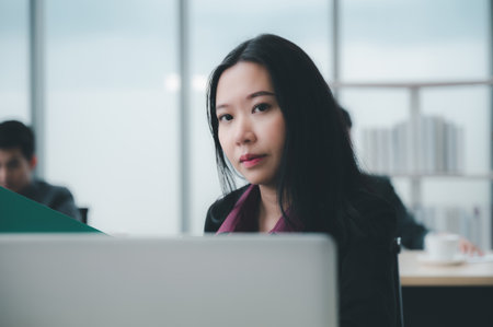 Confident and smart beautiful businesswoman in formal attire stands in the office. With a group of friends and laptop in the background. A cheerful idea to work within the workspace.の写真素材