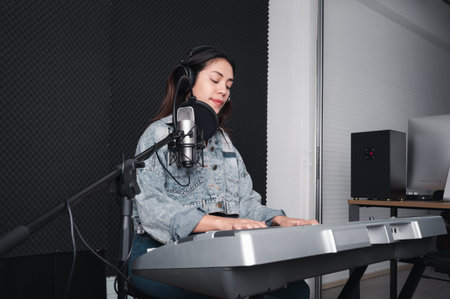 Asian female singer with a passion for music and microphone. While playing her guitar in a professional studio. Music concept, sound recording concept.の写真素材