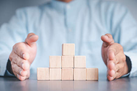 Businessman wearing a blue shirt, arranging the empty wooden blocks with his hands. Which is placed on a white wooden table. Business strategy and action plan. Copy space.の写真素材