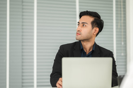 Bearded businessman in a suit is using a laptop in a working room.