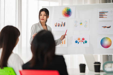 Asian businesswoman in suit discussing or meeting with boss listening to company success report in conference room and stock chart board.の写真素材