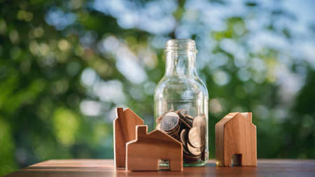 wooden houses and and a glass jar with coins. The concept of buying a house,rent and taxes money on real estate business. with natural green backgroundの写真素材
