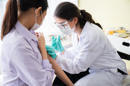 A female doctor or nurse wearing a mask, glove, and face shield are injecting the coronavirus 19...