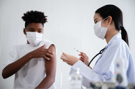 Female doctor or nurse preparing   vaccination for African-American man waiting to be vaccinated in the laboratory.の写真素材