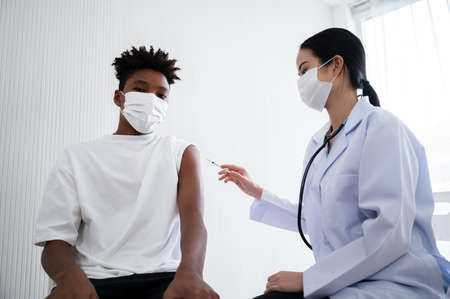 Female doctor or nurse vaccinating  at the shoulders African-American man. By wearing a mask at all times.の写真素材