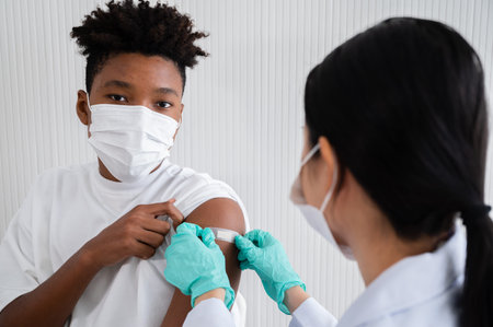 Female doctor or nurse stuck a plaster bandage with for African-American man. After vaccination...