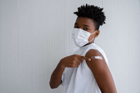 American-African man wearing masks standing show plaster bandage at shoulder make hand sign OK. After vaccine protection  for immunization.の写真素材
