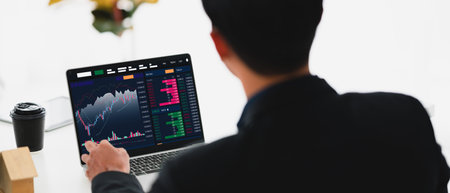 Young money businessman sitting staring at a computer screen displaying a cryptocurrency featuring...