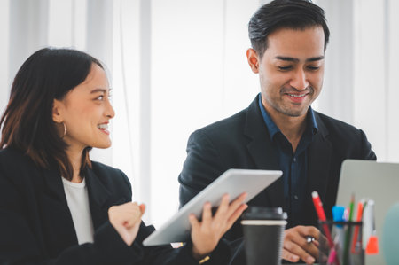 Businesswoman discussing charts and graphs showing on tablet screen with friend with smiling faces in the meeting room. Brainstorming and teamwork concept.の写真素材