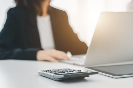 businessman analyzing data on laptop with a business woman using a calculator at the office. Model houses and banknotes.の写真素材