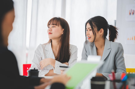 Businesswoman discussing charts and graphs showing on tablet screen with friend with smiling faces in the meeting room. Brainstorming and teamwork concept.の写真素材