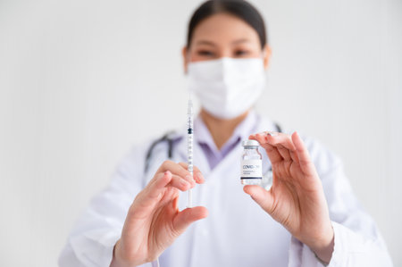 Female doctor wearing a mask stands holding a syringe with a vaccine. Coronavirus19 in the laboratory. Concept of protection against the COVID-19 virus.の写真素材