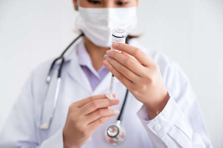 Female doctor wearing a mask stands holds a syringe with a bottle of vaccine for protection Coronavirus19 in a laboratory. Concept of preventing the spread of COVID-19.の写真素材