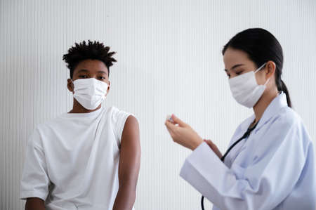 Female doctor or nurse preparing coronavirus 19 vaccination for African-American man waiting to be vaccinated in the laboratory. Concept of preventing the spread of COVID-19.の写真素材