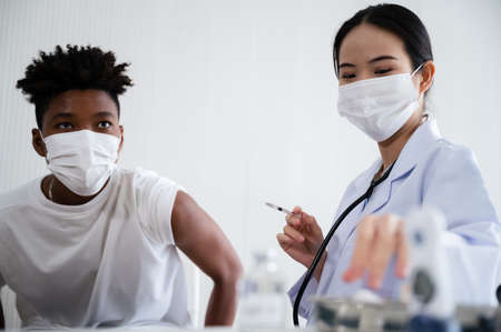 Female doctor or nurse preparing coronavirus 19 vaccination for African-American man waiting to be vaccinated in the laboratory. Concept of preventing the spread of COVID-19.の写真素材
