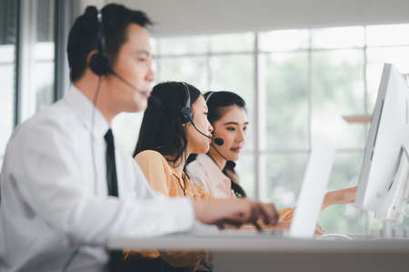 Team of call center staff in Asia wearing headphones with microphones. Stress and headaches while serving customers at desks and computers. Service concept and consulting. communication concept.の写真素材