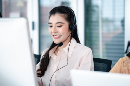 Team of call center staff in Asia wears headphones with a microphone. Smile while serving customers at desks and computers. Service concept and consulting. Communication concept.の写真素材