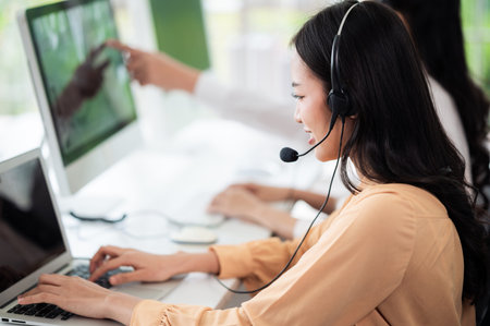 Team of call center staff in Asia wears headphones with a microphone. Smile while serving customers at desks and computers. Service concept and consulting. Communication concept.の写真素材