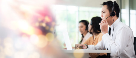 Team of call center staff in Asia wearing headphones with microphones. Stress and headaches while serving customers at desks and computers. Service concept and consulting. communication concept.の写真素材