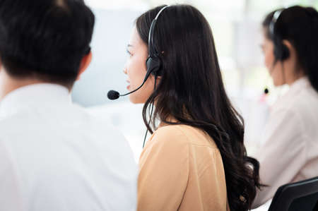 Team of call center staff in Asia wears headphones with a microphone. Smile while serving customers at desks and computers. Service concept and consulting. Communication concept.の写真素材