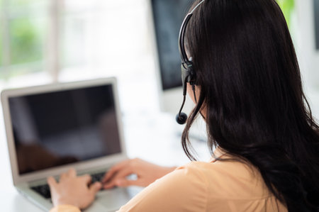 Team of call center staff in Asia wears headphones with a microphone. Smile while serving customers at desks and computers. Service concept and consulting. Communication concept.の写真素材