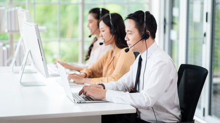 Team of call center staff in Asia wears headphones with a microphone. Smile while serving customers at desks and computers. Service concept and consulting. Communication concept.の写真素材