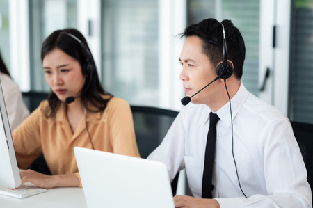 Team of call center staff in Asia wearing headphones with microphones. Stress and headaches while serving customers at desks and computers. Service concept and consulting. communication concept.の写真素材
