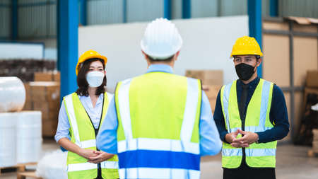 The factory employee consists of engineers, foreman, technicians, and related department staff. Wear a mask, hard hat, and vest. meeting before starting work inside the warehouse. Teamwork concept.の写真素材