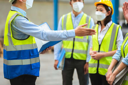 The factory employee consists of engineers, foreman, technicians, and related department staff. Wear a mask, hard hat, and vest. meeting before starting work inside the warehouse. Teamwork concept.の写真素材