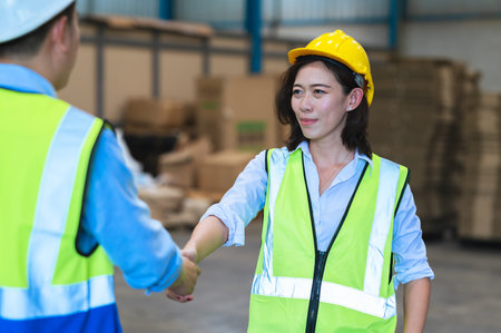 Factory employee of engineers, foreman, technicians and staff. Wear a mask, hard hat, and vest. shake hands to make a deal or celebrate success in the organization or warehouse. Teamwork concept.の写真素材