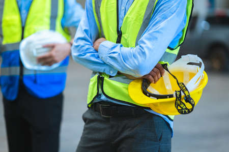 The factory employee consists of engineers, foreman or technicians. Standing holding a hard hat and wear a vest. Stand to pose in line looking focus at the camera. Teamwork concept.の写真素材