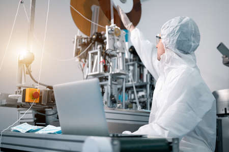 Scientists wearing protective clothing Inspect mask making machines in a laboratory at an industrial plant. Anti-virus production warehouse.の写真素材