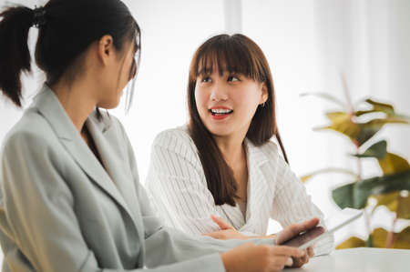 Businesswoman discussing charts and graphs showing on tablet screen with friend with smiling faces in the meeting room. Brainstorming and teamwork concept.の写真素材