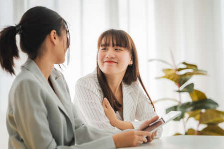 Businesswoman discussing charts and graphs showing on tablet screen with friend with smiling faces in the meeting room. Brainstorming and teamwork concept.の写真素材