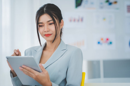 Businesswoman discussing charts and graphs showing on tablet screen with friend with smiling faces in the meeting room. Brainstorming and teamwork concept.の写真素材